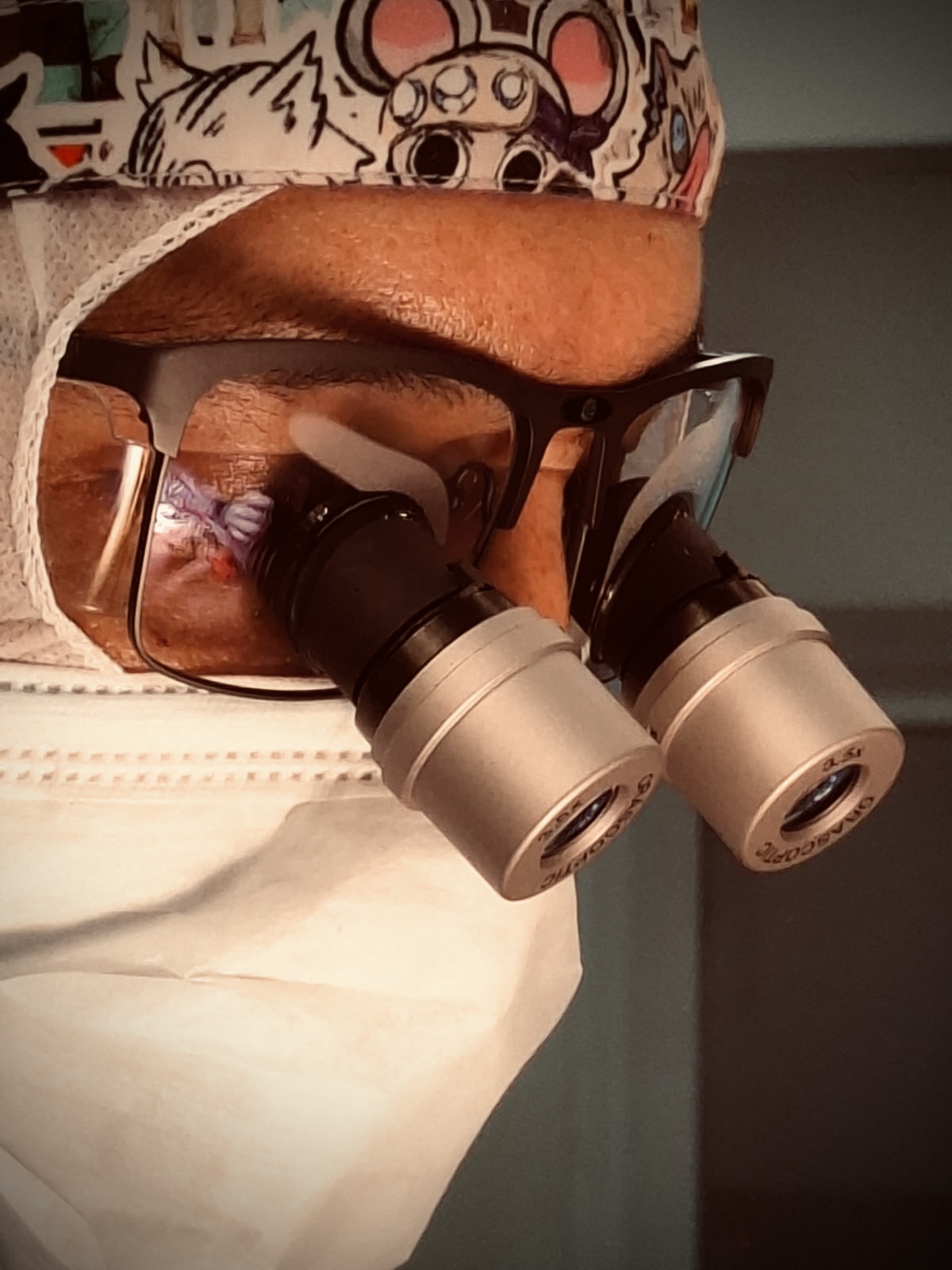 Acercamiento de un médico con mascarilla, gorro y lupas de magnificación